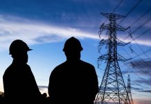 Delays in Australia’s energy transition are hurting workers Energy industry workers in shadows with transmission tower in background (jobs)