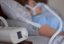 EnergyAustralia fined for alleged life support process failures woman wears CPAP mask connected to machine beside bed (life support)