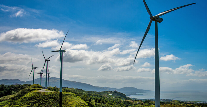 Wind turbines along green mountain ridge with blue sky in background (equis)