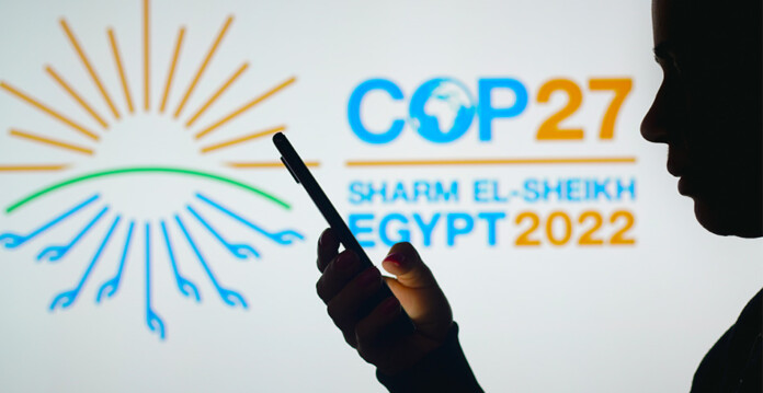 Shadow of person looking at smartphone with COP27 signage illuminated in background (Australia)