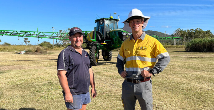 Josh Roncato and Matt Oar standing in front of agricultural sprayer machine with powerlines in background (look up and live)