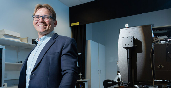 HB11 Energy Founder & Managing Director Dr Warren McKenzie wearing a suit standing in a laser fusion lab (journal)