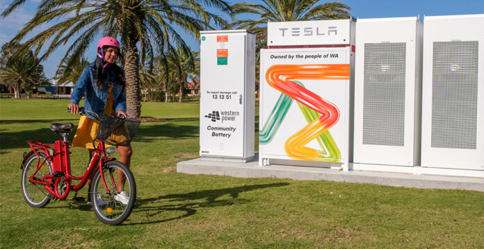 Young girl rides bicycle through park with community batteries in the background