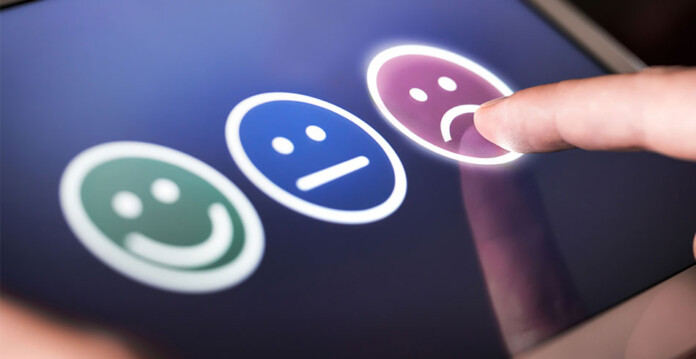 Computerised survey screen with happy, sad and neutral reactions, and finger pointing to sad reaction (consumer confidence)