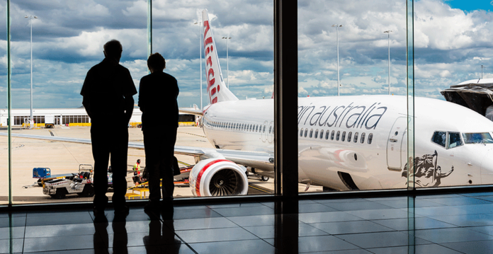 Melbourne-Airport A man and woman stand at windows overlooking the tarmac at Melbourne Airport (AGL flexible demand)