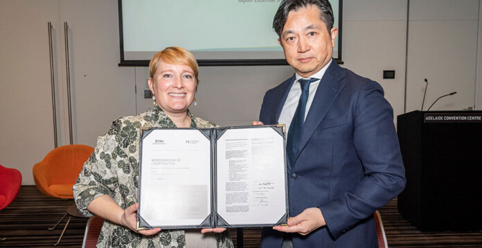 Smiling blonde woman and serious-looking Japanese man hold signed Memorandum of Collaboration paper in frame (hydrogen japan)