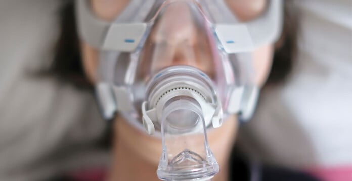 Person wearing CPAP mask with pillow behind them (ergon fined)