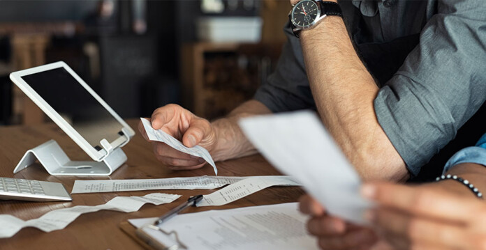 Male small business owner sorts through receipts and bills at desk