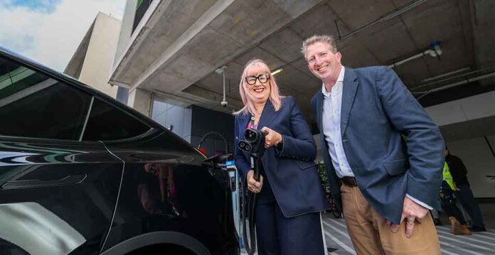 Smiling woman and man holding EV charger up beside electric car