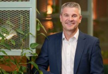 AusNet secures federal funding to trial next-gen grid tech Smiling male executive wearing suit and posing for photo with foliage in the background