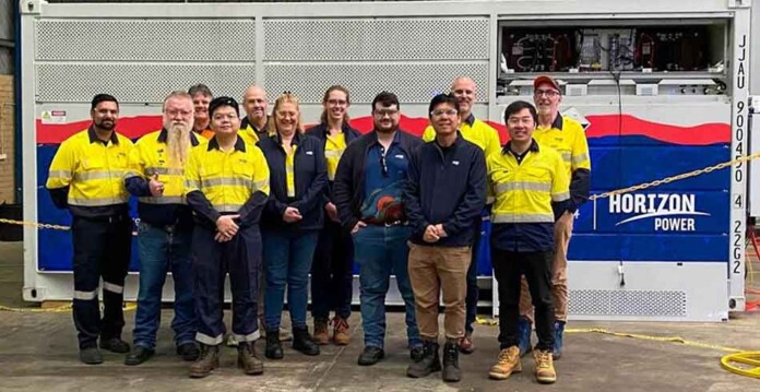 Workers in safety gear pose for group photo in front of large vanadium flow battery with Horizon Power logo