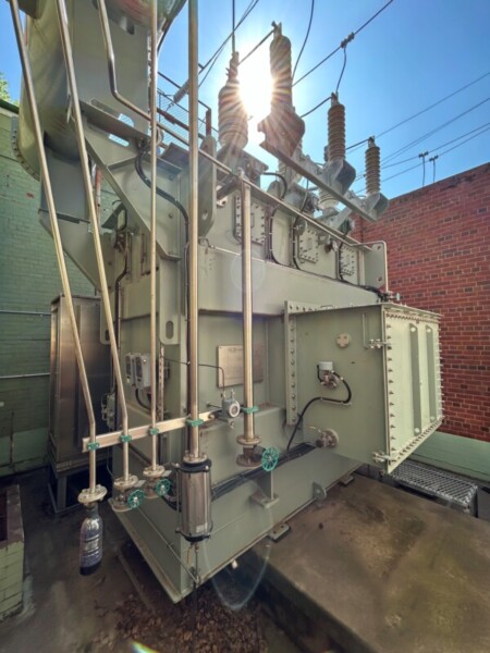 Vegetable oil-filled transformer with brick wall to the right and blue sky above