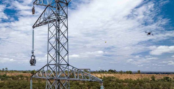 Drone stringing transmission lines between huge towers with blue sky overhead