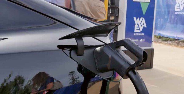 Black electric car being charged with WA EV Network signage behind it