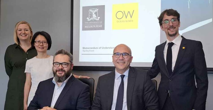 Smiling male and female executives in suits pose for photograph in front of Ocean Winds and University of Melbourne logos on a screen