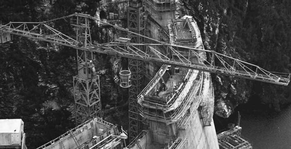 Black and white photo showing construction equipment building dam wall