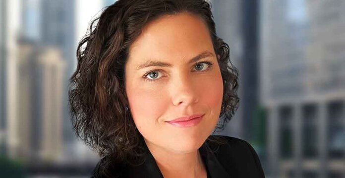 Close-up shot of smiling Laura Caspari with window view of city buildings in background
