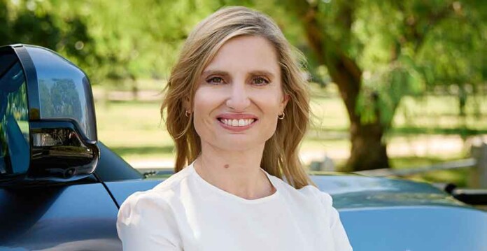 Head and shoulders shot of smiling Julie Delvecchio with electric vehicle and trees in the background