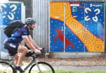 100th community battery installed through ARENA program Cyclist rides past Ausgrid community battery painted with Indigenous artwork
