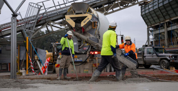 Concrete truck and workers in high-vis safety wear under bridge