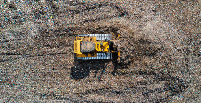 Yellow bulldozer moves garbage at landfill site