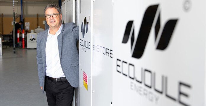 Mike Wishart wears suit and poses for photo next to EcoJoule signage on office wall