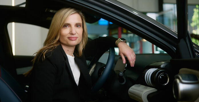 Smiling woman with blonde hair and black suit sits inside an electric vehicle