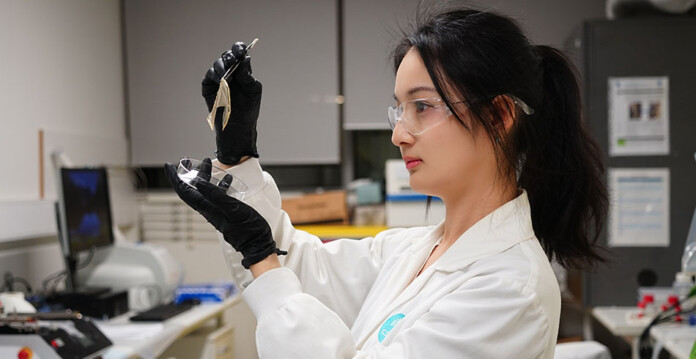 Wanqiao-Liang Young woman in lab coat holds liquid in eyedropper while wearing gloves in lab