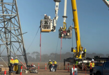 AusNet achieves with Australian-first ISO accreditation Line workers in crane buckets carry out live line work with huge transmission tower in view