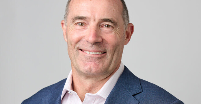 Head and shoulders shot of smiling man wearing suit against grey background