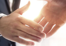 OptiGrid announces new partnership with Acacia Energy Close up of two males shaking hands in front of a window with bright light shining through