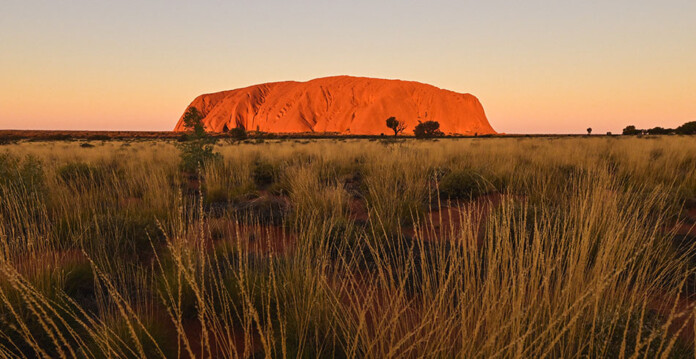 Uluru just before sunset with grasslands in foreground