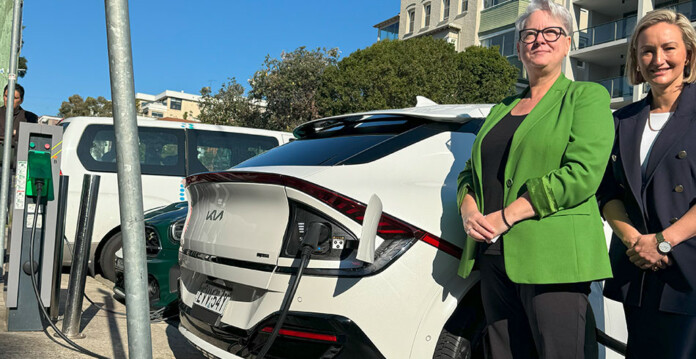 Two women in suits stand beside electric car plugged into a kerbside EV charger