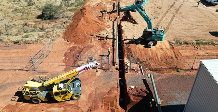 Cranes and other construction equipment work on long gas pipeline, digging a trench in red dirt