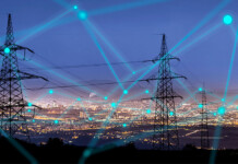 Why the grid is Australia’s true energy challenge Transmission towers with large brightly lit city in the background, with digital concept lines imposed over the top.