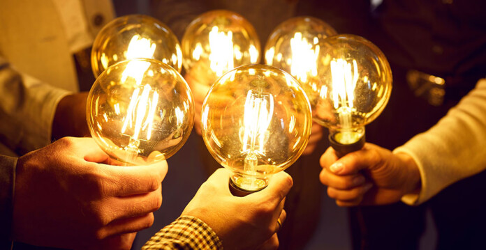 energy-sharing group of people holding lightbulbs clustered together to provide bright light