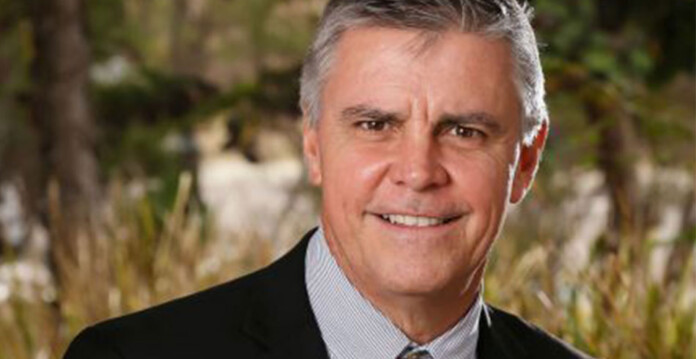 Smiling man with dark grey hair poses for photo in suit and tie