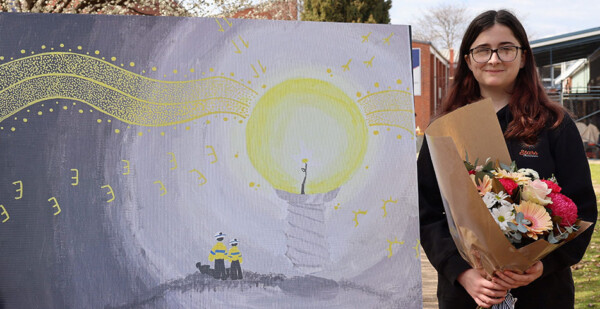 Young female student holds flowers and stands next to artwork
