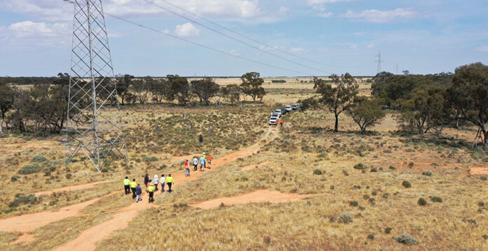 Officials walking on a grassy site with a transmission tower and vehicle in shot
