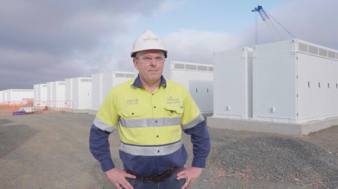Executive in hard hat and safety workwear stands in front of Tesla Megapacks at battery storage project