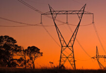 Researchers find best places to build new powerlines Two high-voltage transmission towers with trees underneath and glowing red sky overhead