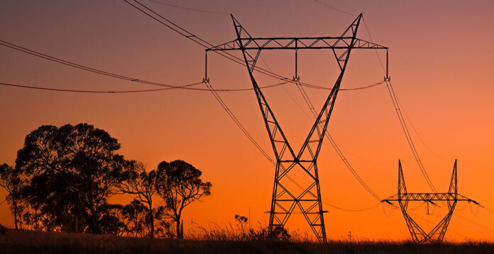 Two high-voltage transmission towers with trees underneath and glowing red sky overhead