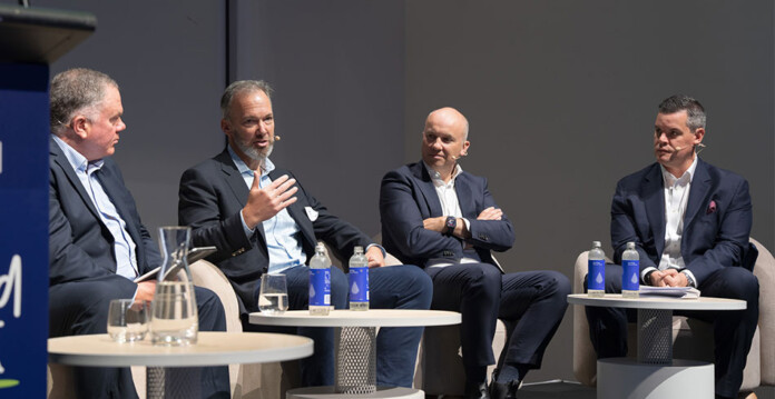 Four men wearing suits participate in discussion panel on a stage
