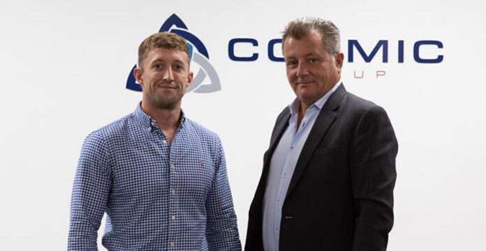 Two men in business attire pose for photo in front of Cosmic Group logo