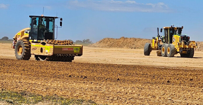 Two yellow graders work on dusty site with blue sky overhead
