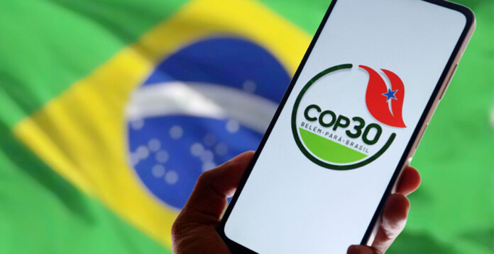 Hand holding a smartphone with COP30 logo in front of Brazilian flag