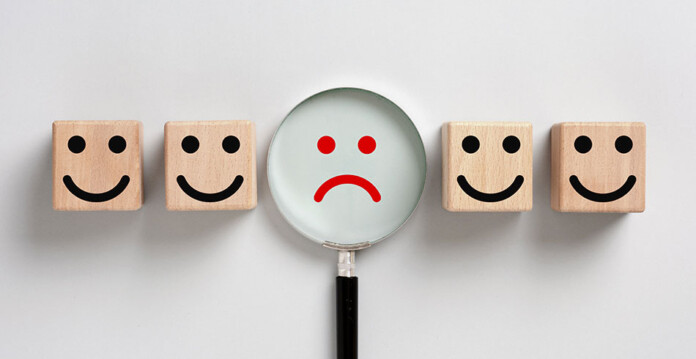 Image depicting frowning face with magnifying glass over it, among four smiling faces