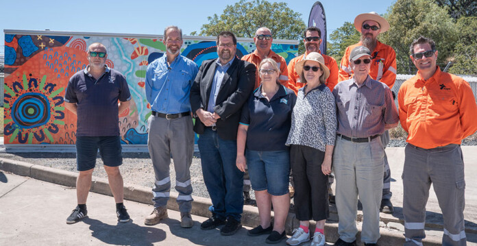 Ausgrid employees and community members pose for photo in front of microgrid painted with Indigenous artwork