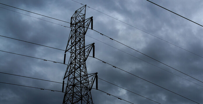 Electricity transmission tower against dark cloudy sky
