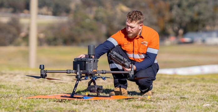 Man in high-vis workwear kneels on the ground with a drone